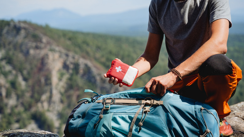 A traveler in the mountains storing a first-aid kit in his backpack.