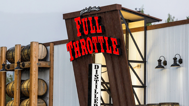 neon sign saying 'distillery grill' on building lined with wooden barrels