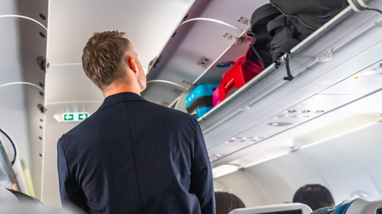 A man staring at a row of full overhead bins
