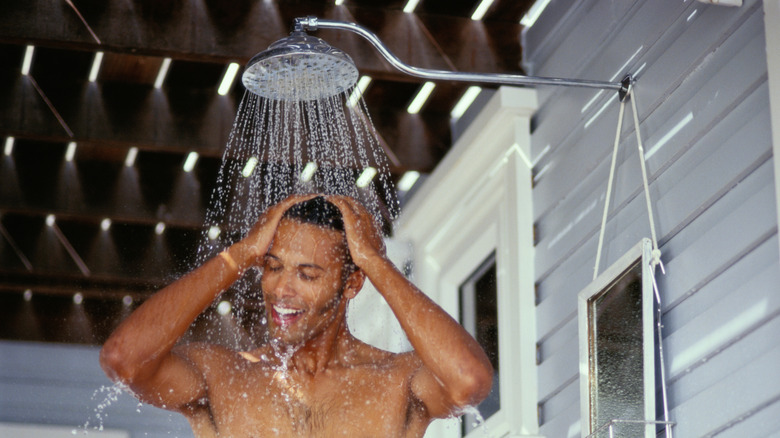 A smiling man showering under a showerhead with his eyes closed