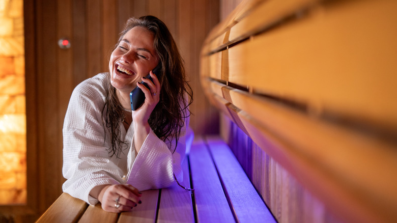 A woman laughing and smiling while using a cell phone to make a call in a sauna