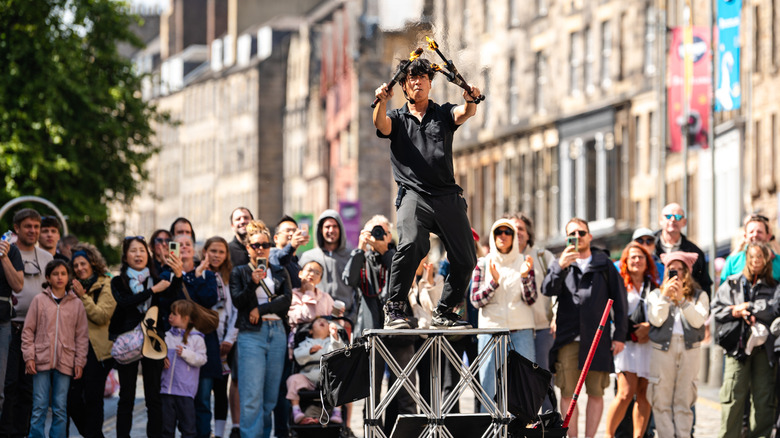 A crowd watches a man on a pedestal with flaming torches during Edinburgh Festival Fringe