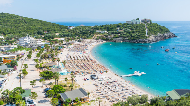 Aerial shot of Albania Riviera, with views of green hills, blue waters, and beach chairs on the sand