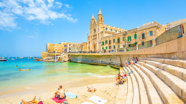 people relaxing at beach by stone staircase and old buildings
