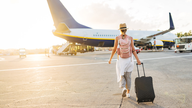 tourist walks toward airplane on tarmac while rolling carry-on suitcase
