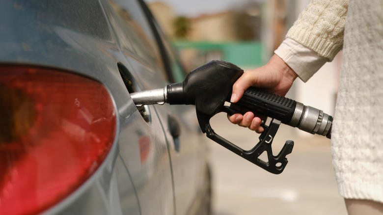 A woman in a knit sweater pumps gas at a gas station in New Jersey.