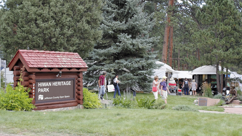 Sign for Hiwan Heritage Park with trees and people in the background