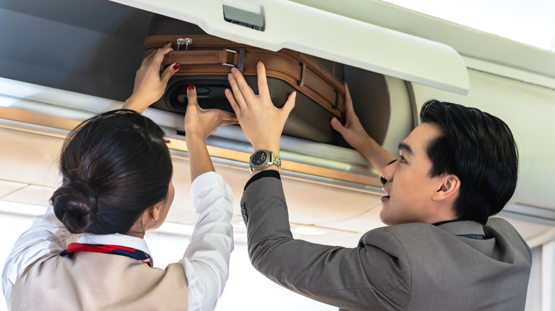 A flight attendant assisting a passenger with their bag