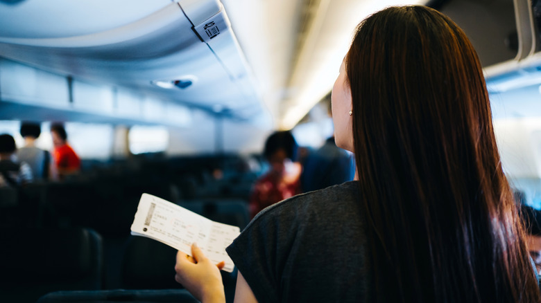 Woman holding boarding pass looking at seats on flight