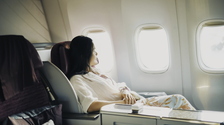 A relaxed business class passenger is looking out of the window of a passenger aircraft.
