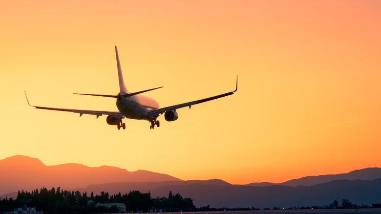 An airplane just after takeoff before a line of hills and a golden sky at sunset