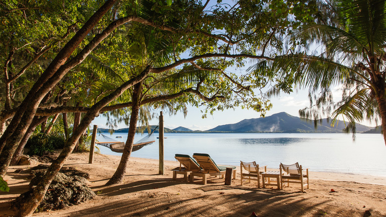Exterior image of beach loungers and a hammock, surrounded by tropical foliage on a white-sand beach facing the Fijian archipelago, at Turtle Island resort in Fiji during the day