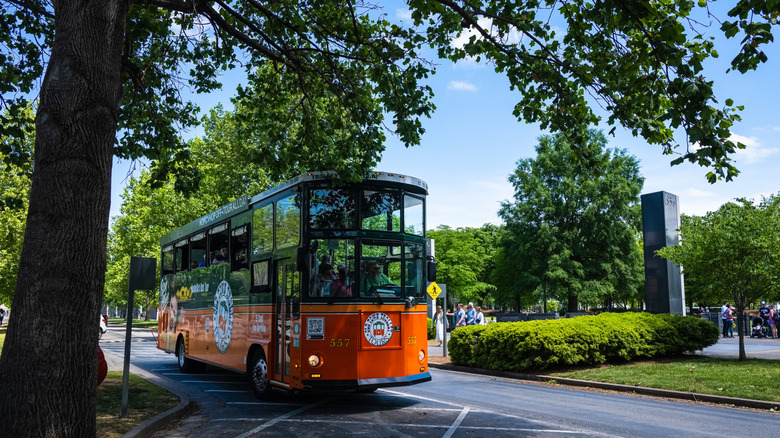 An orange and green old town trolley bus driving past a Nashville park