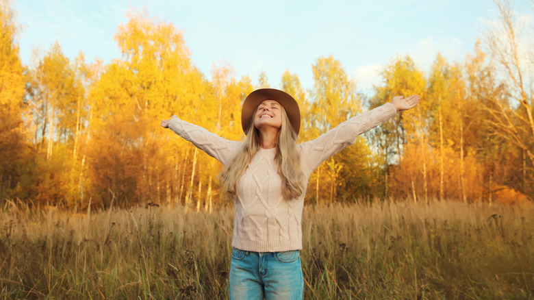 A woman throws her arms back in excitement amidst fall foliage