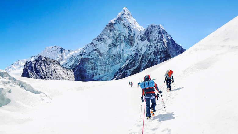 Climbers trekking through a snowy slope heading to Mount Everest in the distance