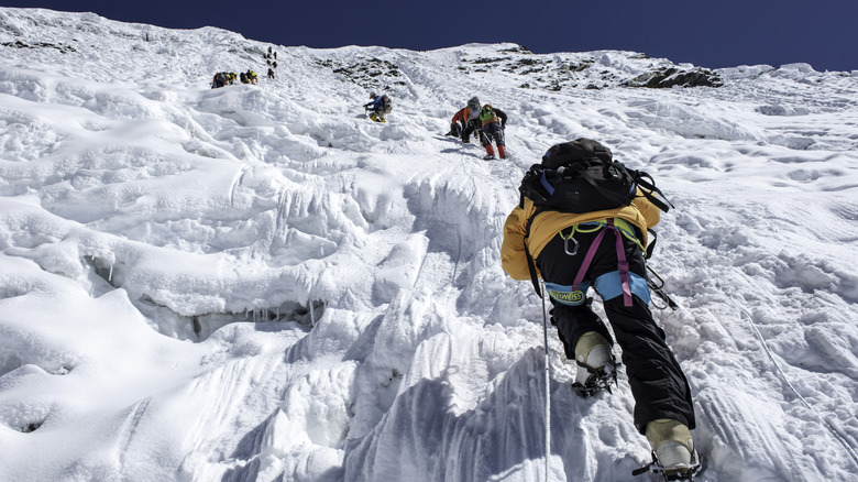 A line of mountaineers using rope and crampons attempts to scale a Himalayan ice wall