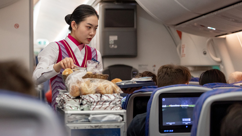 Flight attendant pushes food trolley with meals and snacks for passengers during in-flight service