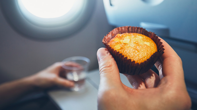 Close-up image of passenger holding muffin in one hand and glass of water in other on flight