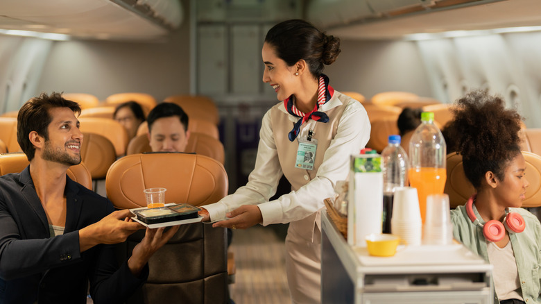 A flight attendant serving a passenger a meal
