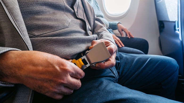 A man buckling his seatbelt on a plane