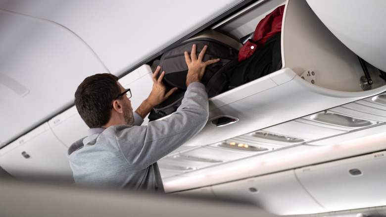 Person stuffing bag in overhead bin