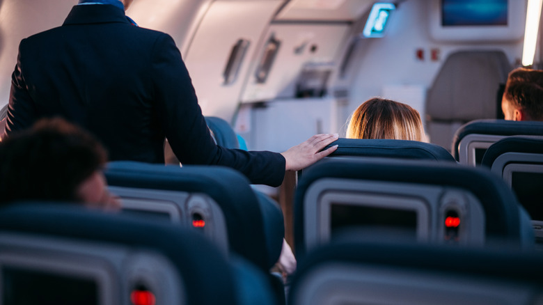 flight attendant in aisle of plane with hand on seat