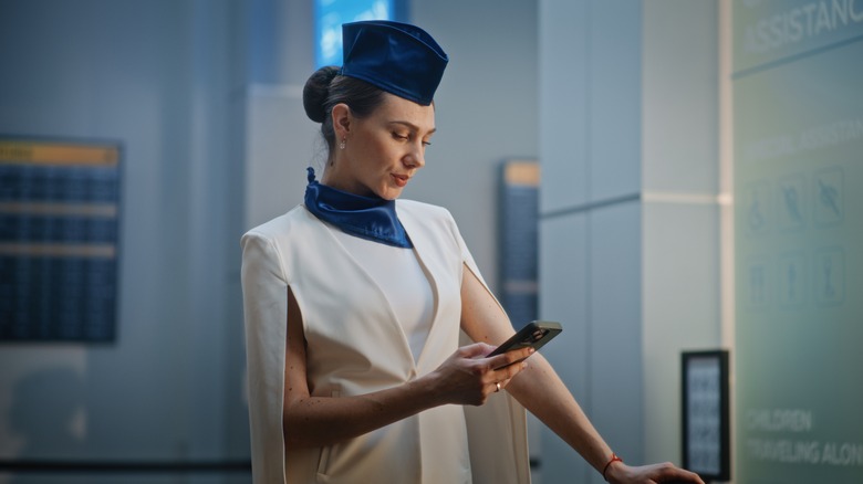 Smartly dressed flight attendant looks at smartphone in an airport