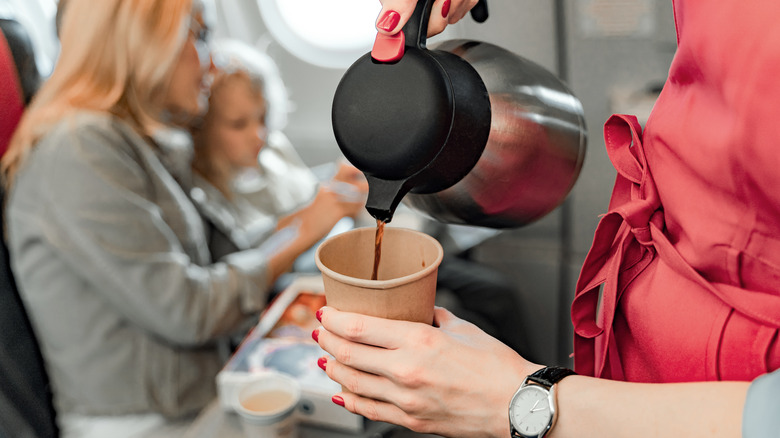 A flight attendant pours coffee into a cardboard cup onboard an airplane