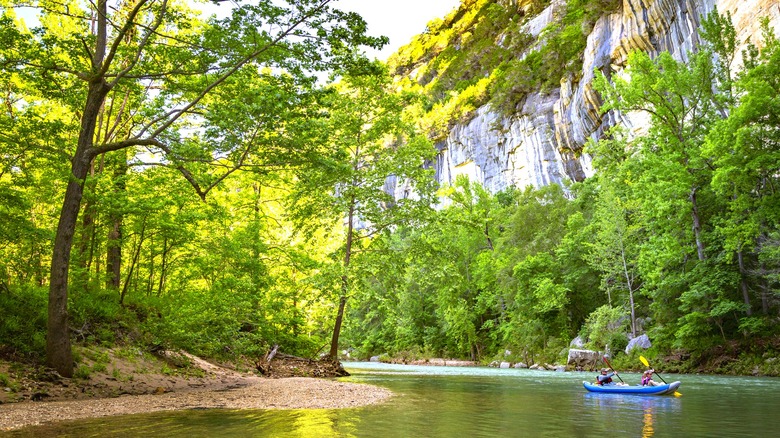 A blue kayak on Buffalo National River in Arkansas shaded by high stone cliffs and forested banks