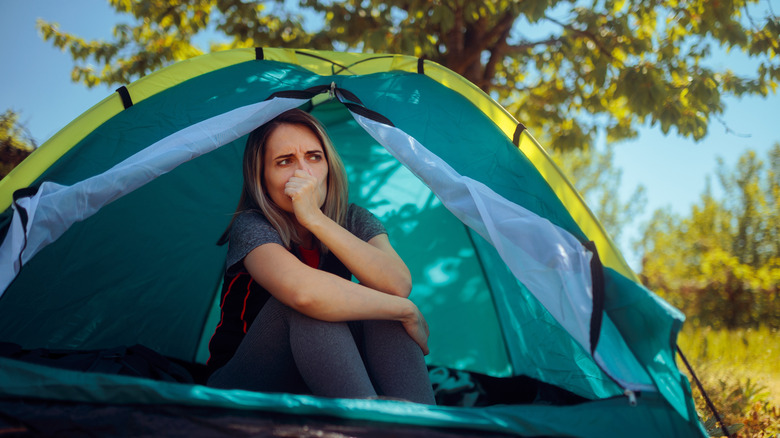 An unhappy female camper sitting in her tent looking frustrated