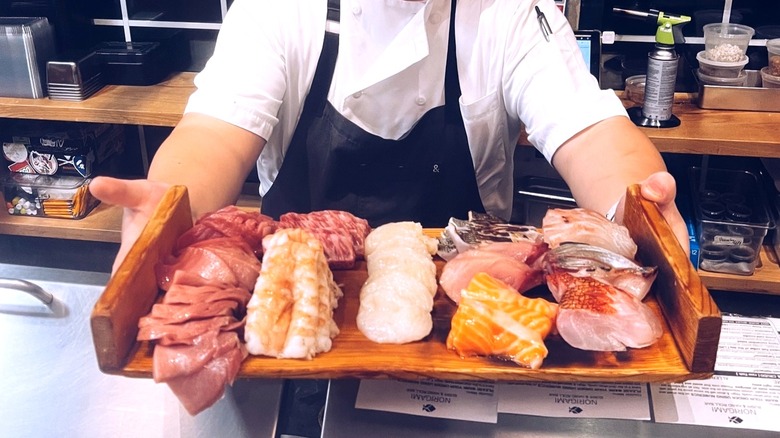 The chef at Norigami FL displaying a wooden tray of raw fish