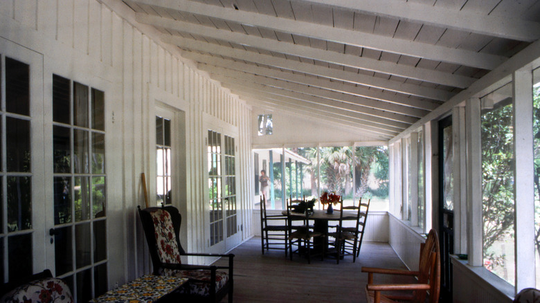 Screen covered porch of a white wood panel home