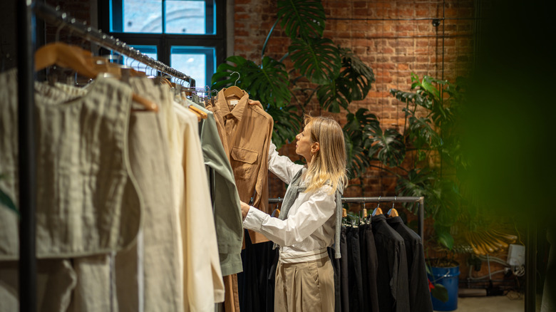 A woman browsing garments in a small clothing store with plants.