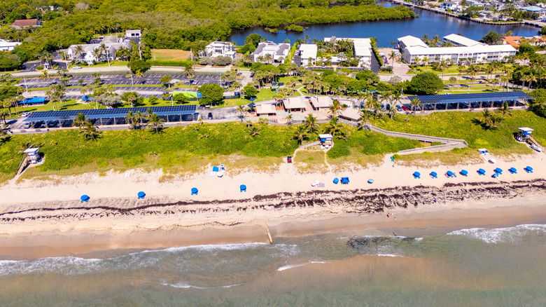 Aerial photo of Oceanfront Park with white sand, waves, boardwalk, umbrellas, and homes and canals behind it