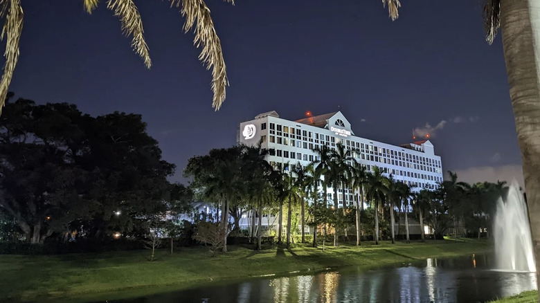 Nighttime view of DoubleTree by Hilton Deerfield Beach Boca Raton with palm tree fronds in foreground and fountain