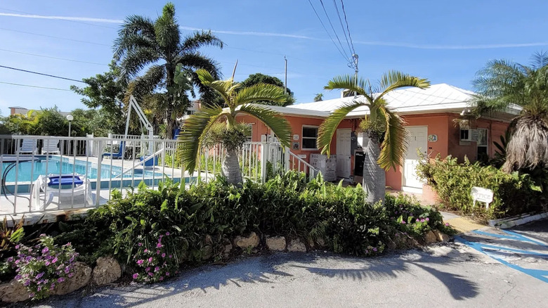 View of coral guest room building, tropical landscaping, and pool area at Sea Dell Motel in Marathon, Florida