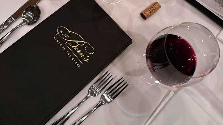 A Bern's Steak House wine menu with a glass of red wine beside it