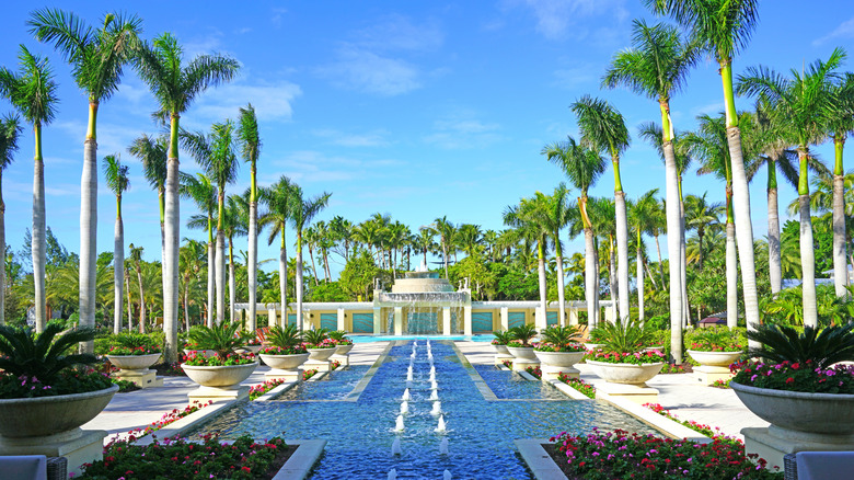 A long fountain with trees and flowers around it and the Hyatt Regency Coconut Resort & Spa Waterfall Pool in the distance.