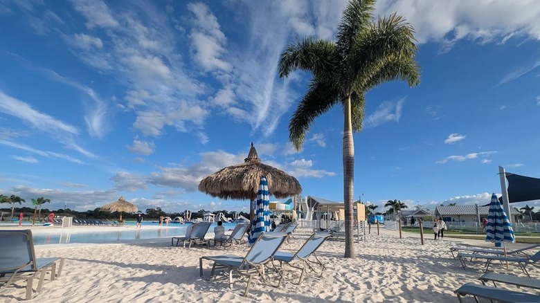 Chairs and a tiki-style umbrella on a sandy stretch of land with a blue sky overhead