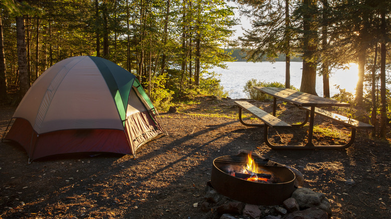 Camping site with tent, table, and fire by the lake