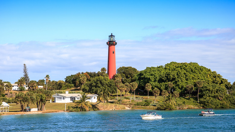 The Jupiter Inlet Lighthouse with surrounding waters, homes, foliage, and boats passing by