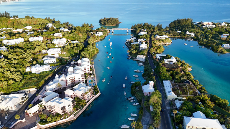 View of a road bridge, residential homes among greenery, boats, and turquoise waters along the Bermuda coast