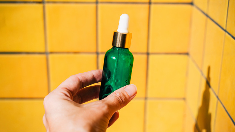 Hand holding a dropper bottle in a bathroom