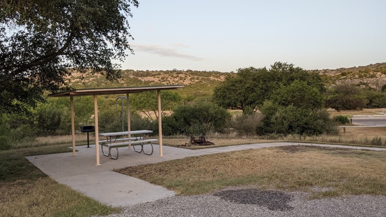 A campsite with a shade pavilion, grill, fire ring, and picnic table at Kickapoo Cavern State Park
