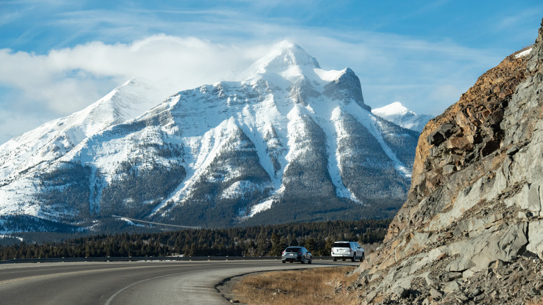 Cars driving on Highway 3, with snow-capped mountains in the distance, in Crowsnest Pass in Alberta, Canada