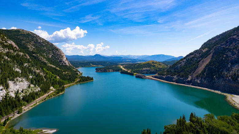 Blue alpine lake surrounded by mountains, with a blue, cloudy sky above, in Crowsnest Pass in Alberta, Canada