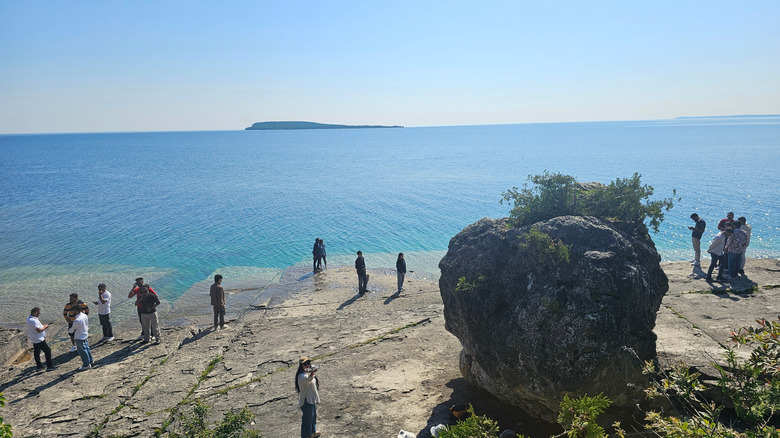Travelers cluster near a giant border on a rocky shore on a sunny day in Fathom Five National Marine Park, Canada