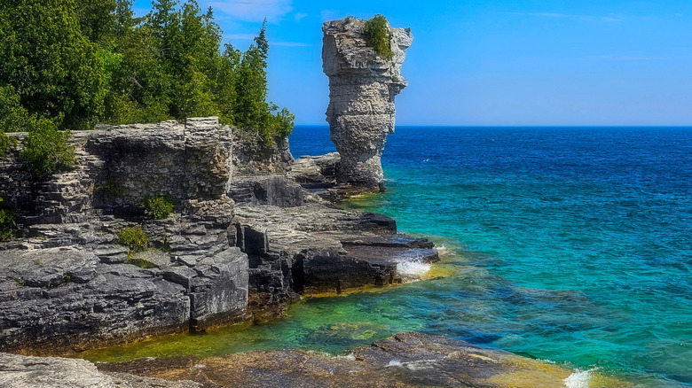 A tower-like rock formation hovers above turquoise waters on a sunny day in Fathom Five National Marine Park, Canada