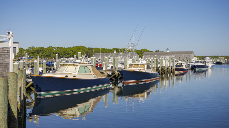 Small motorboats docked at wooden slips in a quiet, sunny coastal marina in Barnstable, Massachusetts