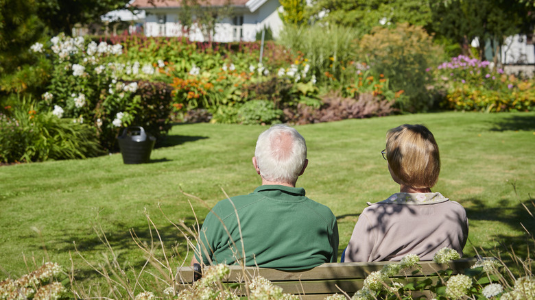 An elderly couple relaxing on a bench in a garden on a sunny day